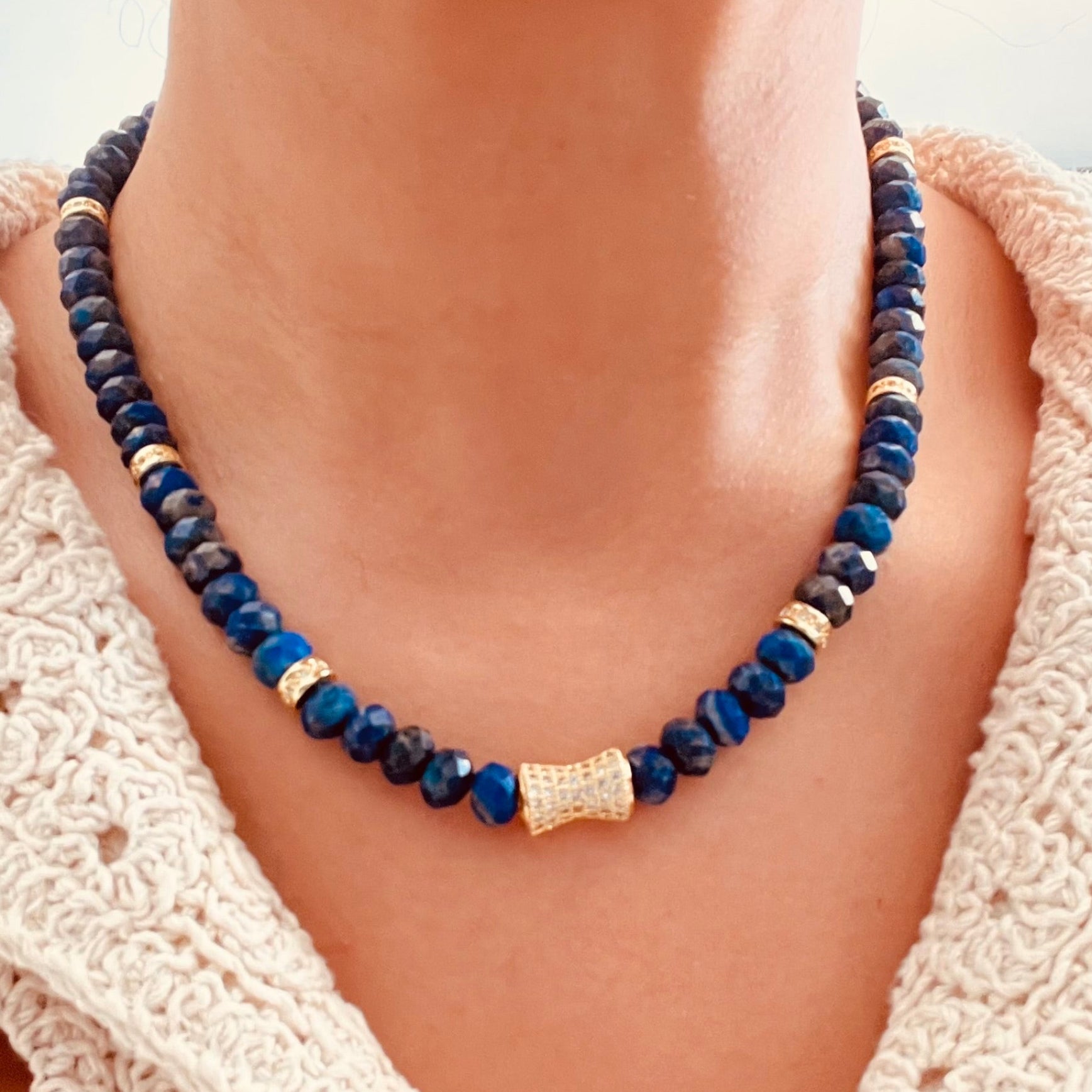 Lapis Lazuli beaded necklace made of dark blue beads with small gold spacer accents and a textured gold center bead, paired with a cream crochet top.