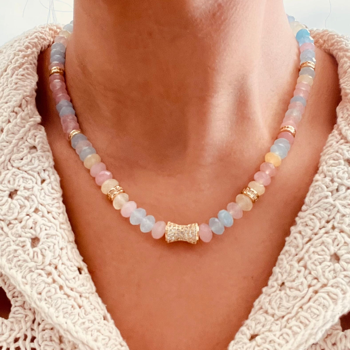 delicate Morganite beaded necklace with pastel-colored round beads and a central textured gold-toned accent, paired with a cream crochet cardigan.